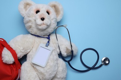Photo of Pediatrics concept. Toy bear with stethoscope and first aid kit on light blue background, top view. Space for text
