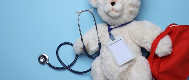 Photo of Pediatrics concept. Toy bear with stethoscope and first aid kit on light blue background, top view. Space for text