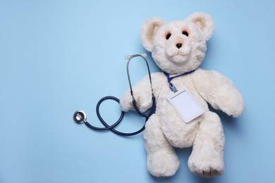 Photo of Pediatrics concept. Toy bear with stethoscope on light blue background, top view. Space for text