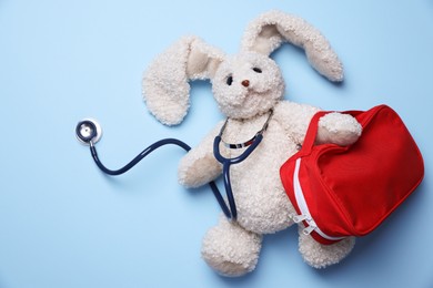 Photo of Pediatrics concept. Toy bunny with stethoscope and first aid kit on light blue background, top view