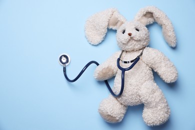 Photo of Pediatrics concept. Toy bunny with stethoscope on light blue background, top view. Space for text