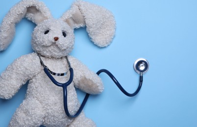 Photo of Pediatrics concept. Toy bunny with stethoscope on light blue background, top view. Space for text