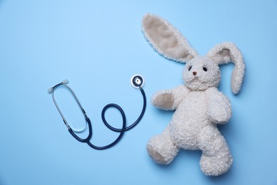 Photo of Pediatrics concept. Toy bunny with stethoscope on light blue background, top view
