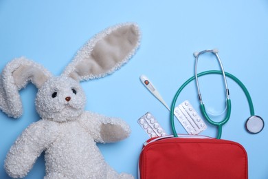 Photo of Pediatrics concept. Toy bunny with stethoscope and first aid kit on light blue background, flat lay