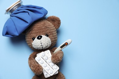 Photo of Pediatrics concept. Toy bear with ice bag, pills and thermometer on light blue background, top view. Space for text
