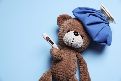 Photo of Pediatrics concept. Toy bear with ice bag and thermometer on light blue background, top view. Space for text