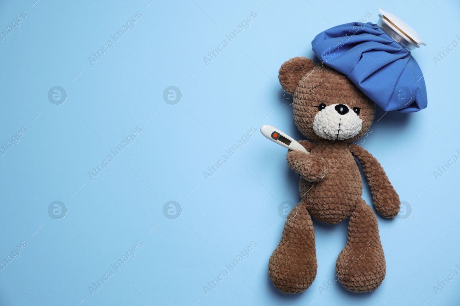 Pediatrics concept. Toy bear with ice bag and thermometer on light blue background, top view. Space for text Photo of Pediatrics concept. Toy bear with ice bag and thermometer on light blue background, top view. Space for text