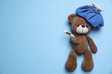 Photo of Pediatrics concept. Toy bear with ice bag and thermometer on light blue background, top view. Space for text