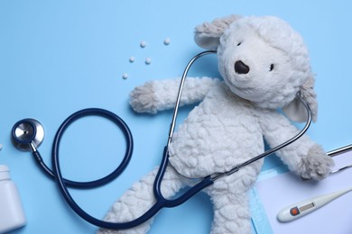 Photo of Pediatrics concept. Toy sheep with stethoscope and pills on light blue background, flat lay