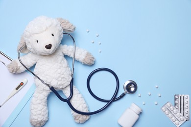 Photo of Pediatrics concept. Toy sheep with stethoscope and pills on light blue background, flat lay. Space for text