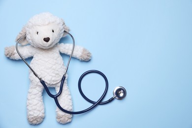 Photo of Pediatrics concept. Toy sheep with stethoscope on light blue background, top view. Space for text