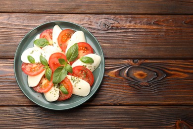 Photo of Tasty salad Caprese with mozzarella, tomatoes, basil and spices on wooden table, top view. Space for text