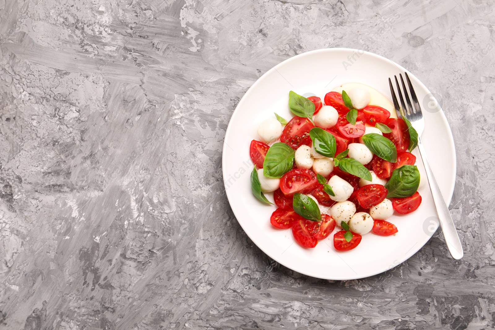 Photo of Tasty salad Caprese with mozzarella, tomatoes, basil and spices on grey table, top view. Space for text