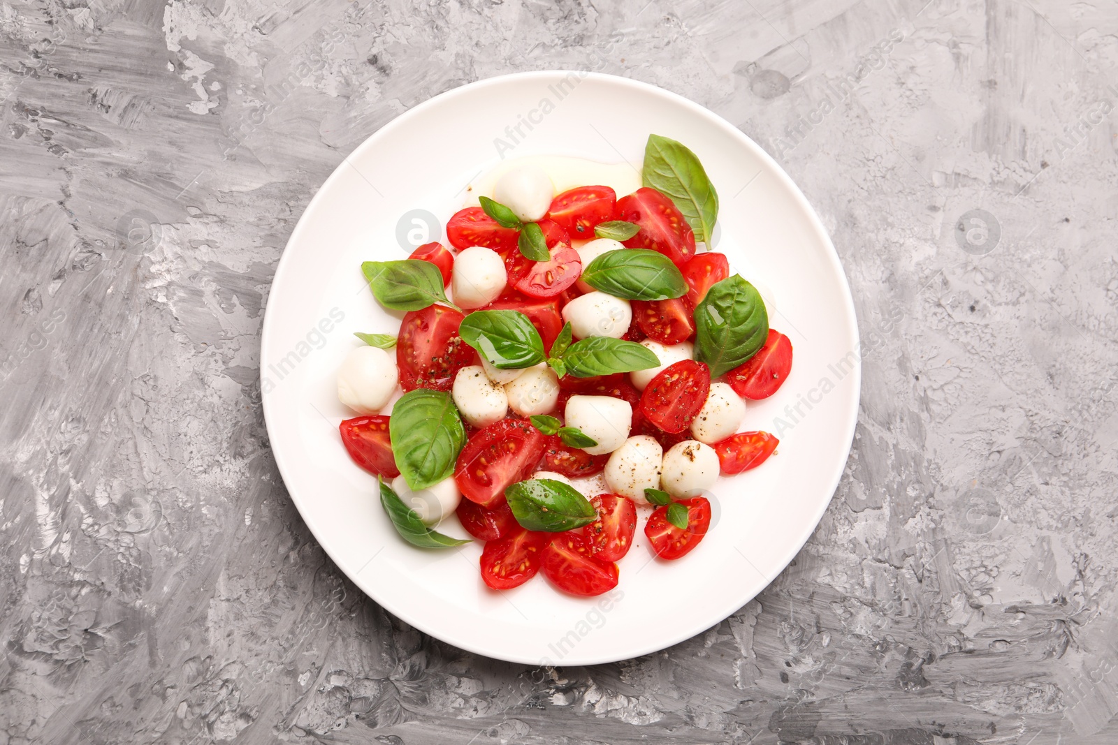 Photo of Tasty salad Caprese with mozzarella, tomatoes, basil and spices on grey table, top view