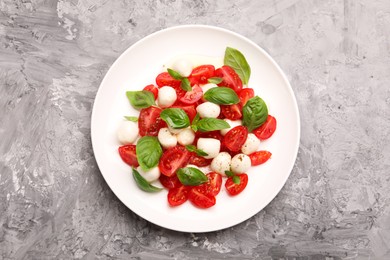 Photo of Tasty salad Caprese with mozzarella, tomatoes, basil and spices on grey table, top view