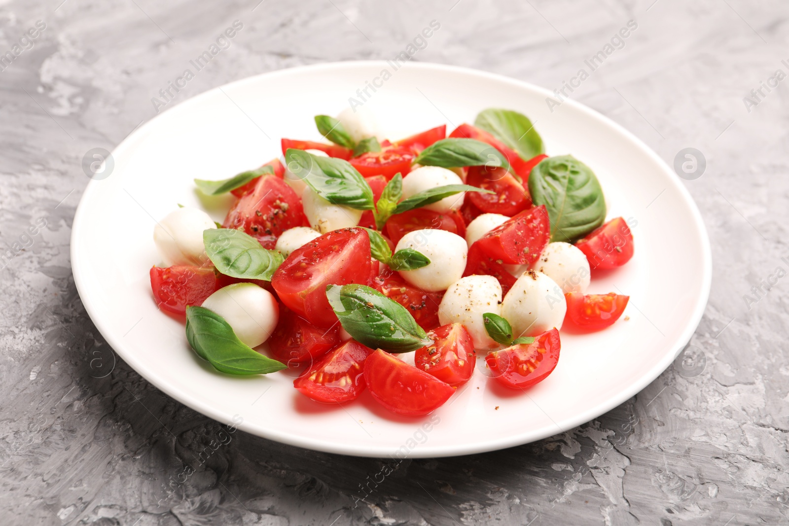 Photo of Tasty salad Caprese with mozzarella, tomatoes, basil and spices on grey table, closeup