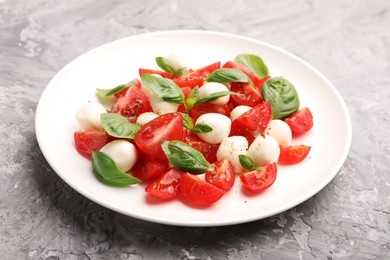 Photo of Tasty salad Caprese with mozzarella, tomatoes, basil and spices on grey table, closeup
