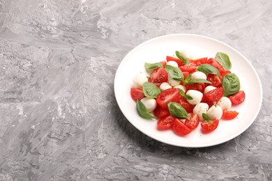 Photo of Tasty salad Caprese with mozzarella, tomatoes, basil and spices on grey table, space for text