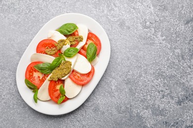 Photo of Tasty salad Caprese with mozzarella, tomatoes, basil and pesto sauce on grey table, top view. Space for text