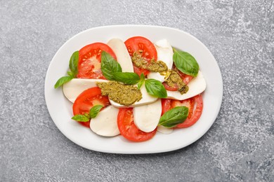 Photo of Tasty salad Caprese with mozzarella, tomatoes, basil and pesto sauce on grey table, top view