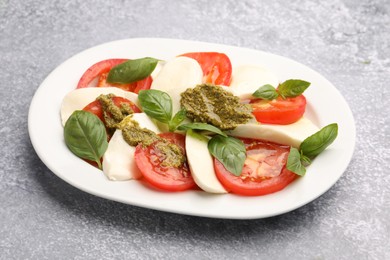 Photo of Tasty salad Caprese with mozzarella, tomatoes, basil and pesto sauce on grey table, closeup