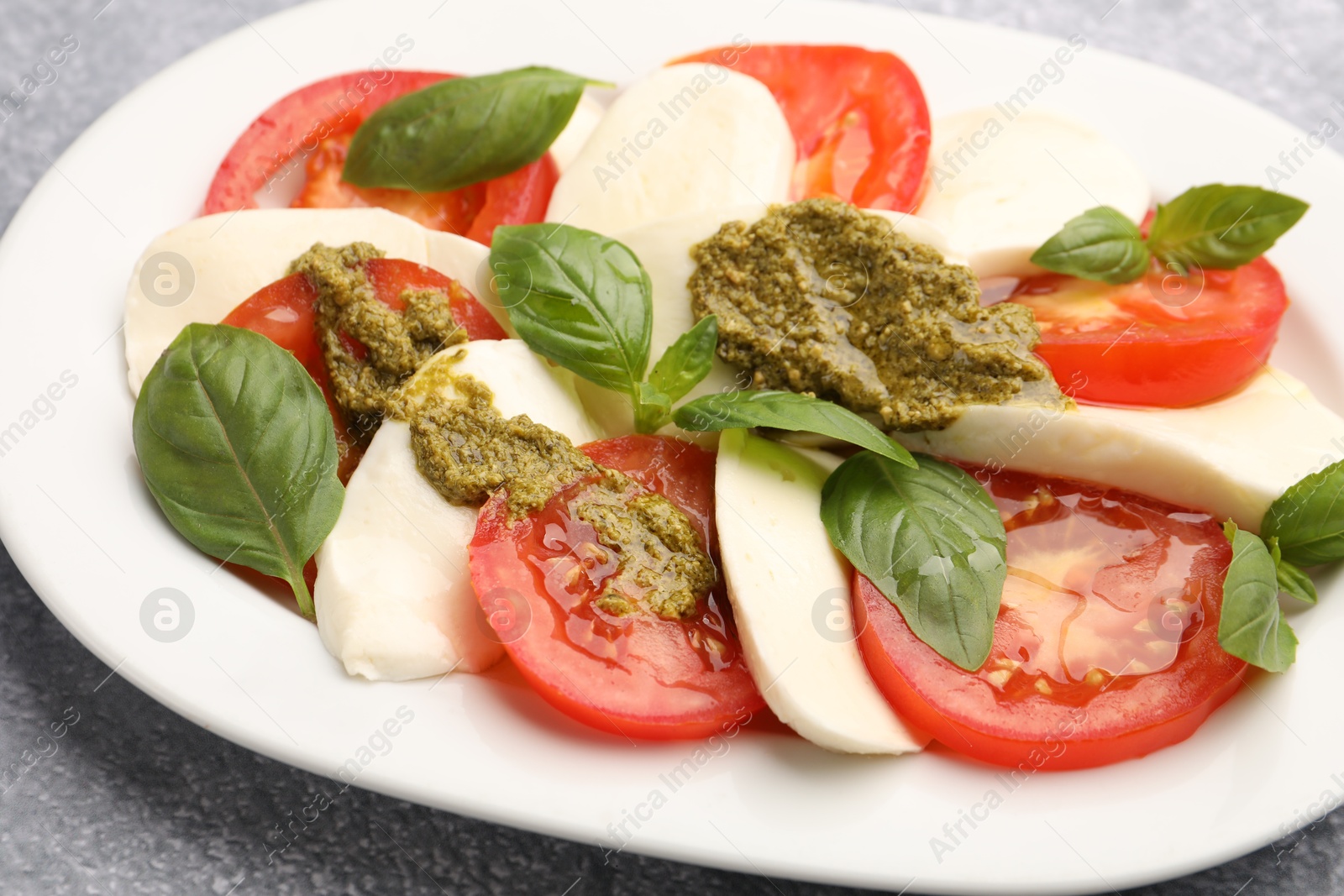 Photo of Tasty salad Caprese with mozzarella, tomatoes, basil and pesto sauce on grey table, closeup