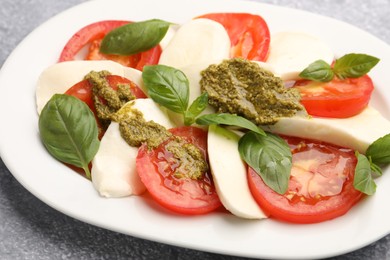 Photo of Tasty salad Caprese with mozzarella, tomatoes, basil and pesto sauce on grey table, closeup