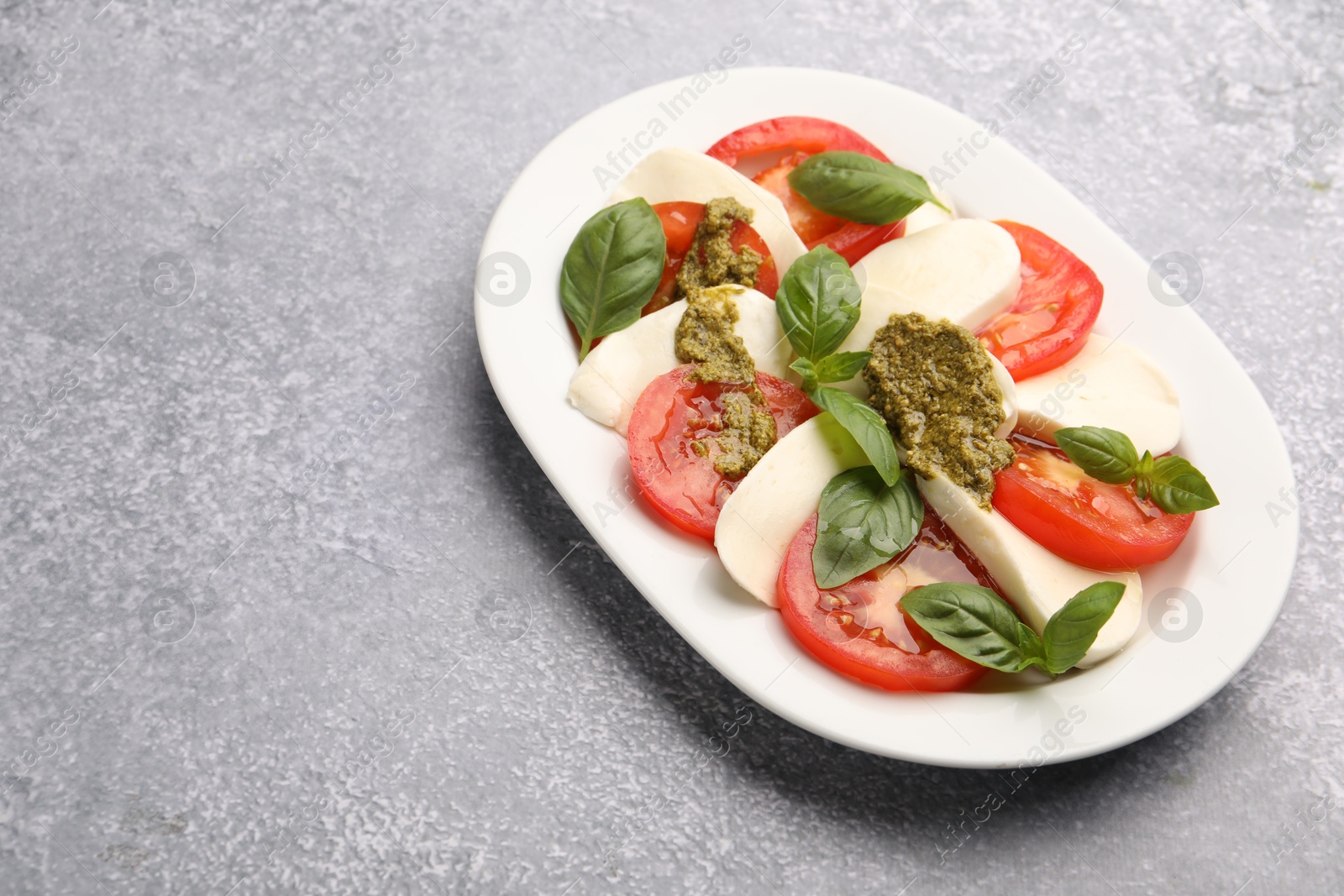 Photo of Tasty salad Caprese with mozzarella, tomatoes, basil and pesto sauce on grey table, closeup. Space for text