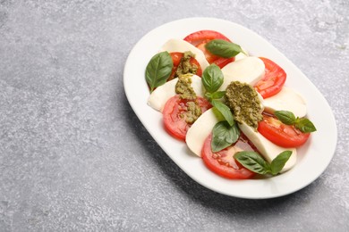 Photo of Tasty salad Caprese with mozzarella, tomatoes, basil and pesto sauce on grey table, closeup. Space for text