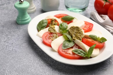 Photo of Tasty salad Caprese served with pesto sauce on grey table, closeup. Space for text
