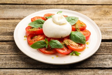 Photo of Tasty salad Caprese with mozzarella, tomatoes, basil and pesto sauce on wooden table, closeup