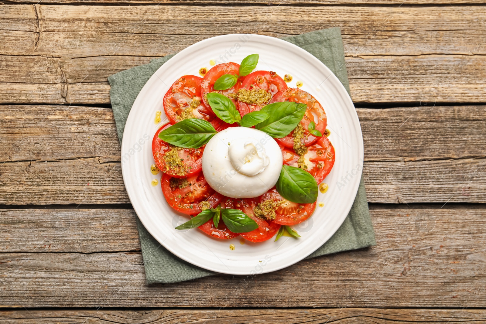 Photo of Tasty salad Caprese with mozzarella, tomatoes, basil and pesto sauce on wooden table, top view