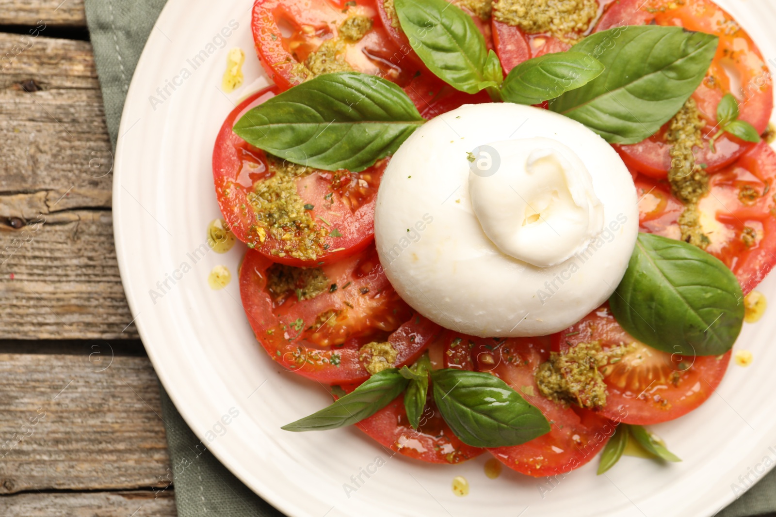 Photo of Tasty salad Caprese with mozzarella, tomatoes, basil and pesto sauce on wooden table, top view