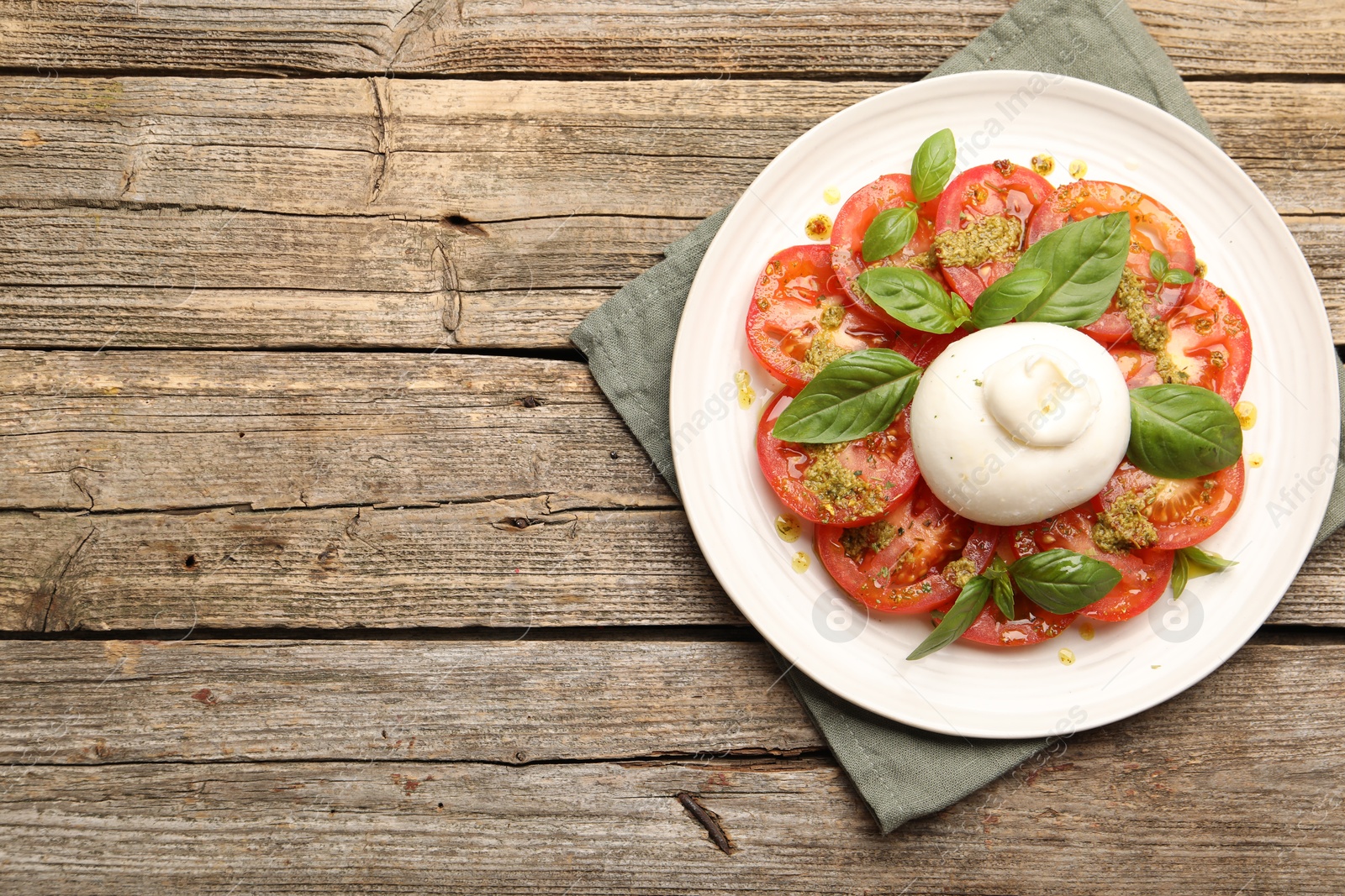 Photo of Tasty salad Caprese with mozzarella, tomatoes, basil and pesto sauce on wooden table, top view. Space for text