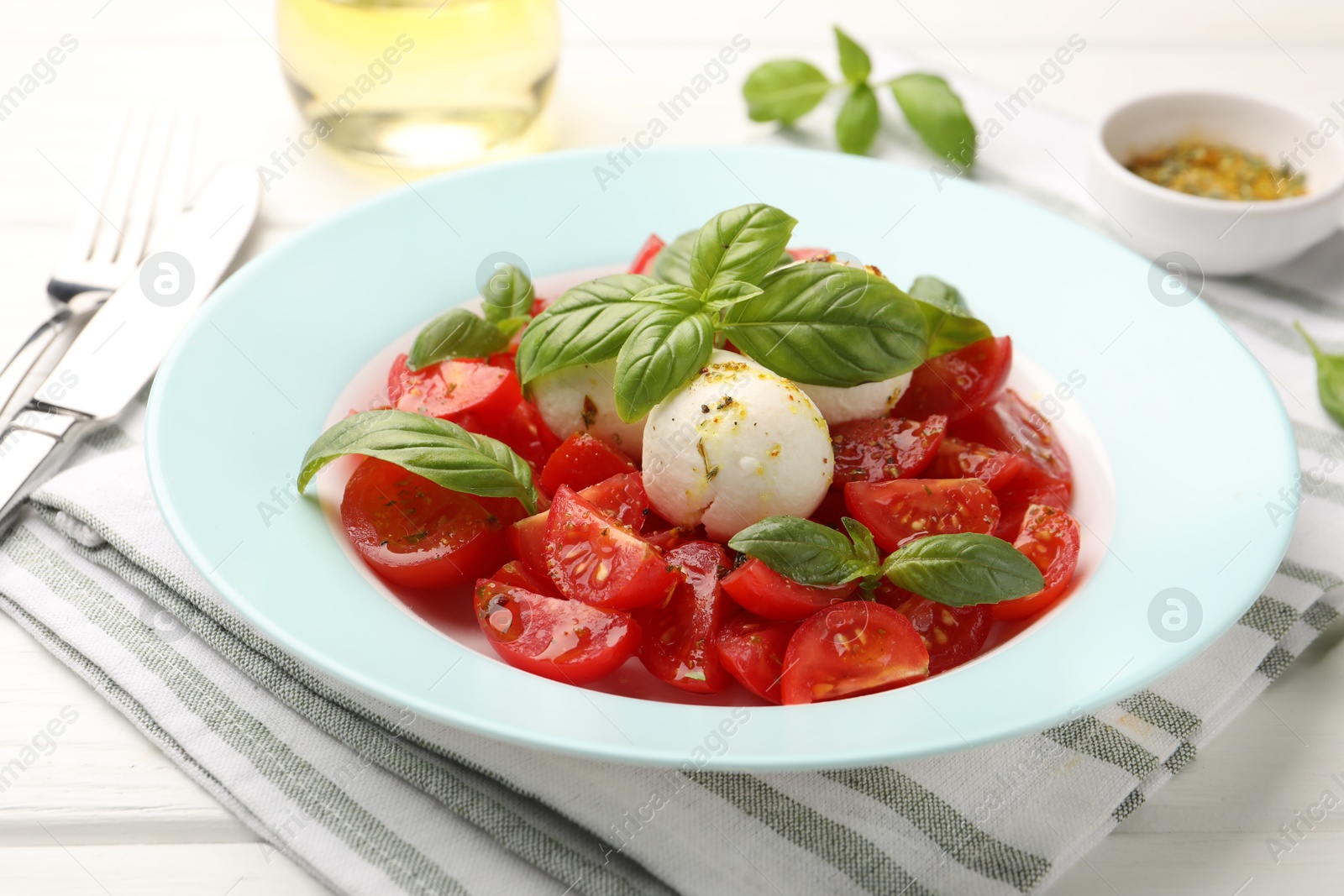 Photo of Tasty salad Caprese with mozzarella, tomatoes, basil and spices on white wooden table, closeup