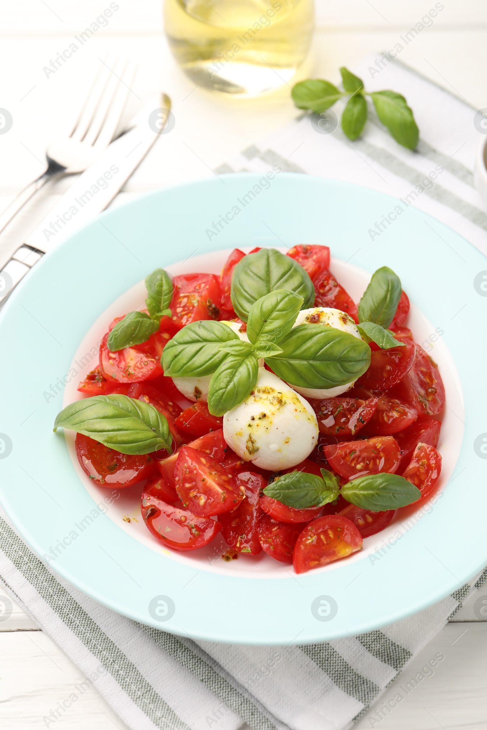 Photo of Tasty salad Caprese with mozzarella, tomatoes, basil and spices on white wooden table, closeup