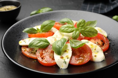 Photo of Tasty salad Caprese with mozzarella, tomatoes, basil and spices on black table, closeup