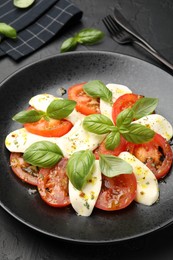 Photo of Tasty salad Caprese with mozzarella, tomatoes, basil and spices on black table, closeup