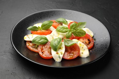 Photo of Tasty salad Caprese with mozzarella, tomatoes, basil and spices on black table, closeup