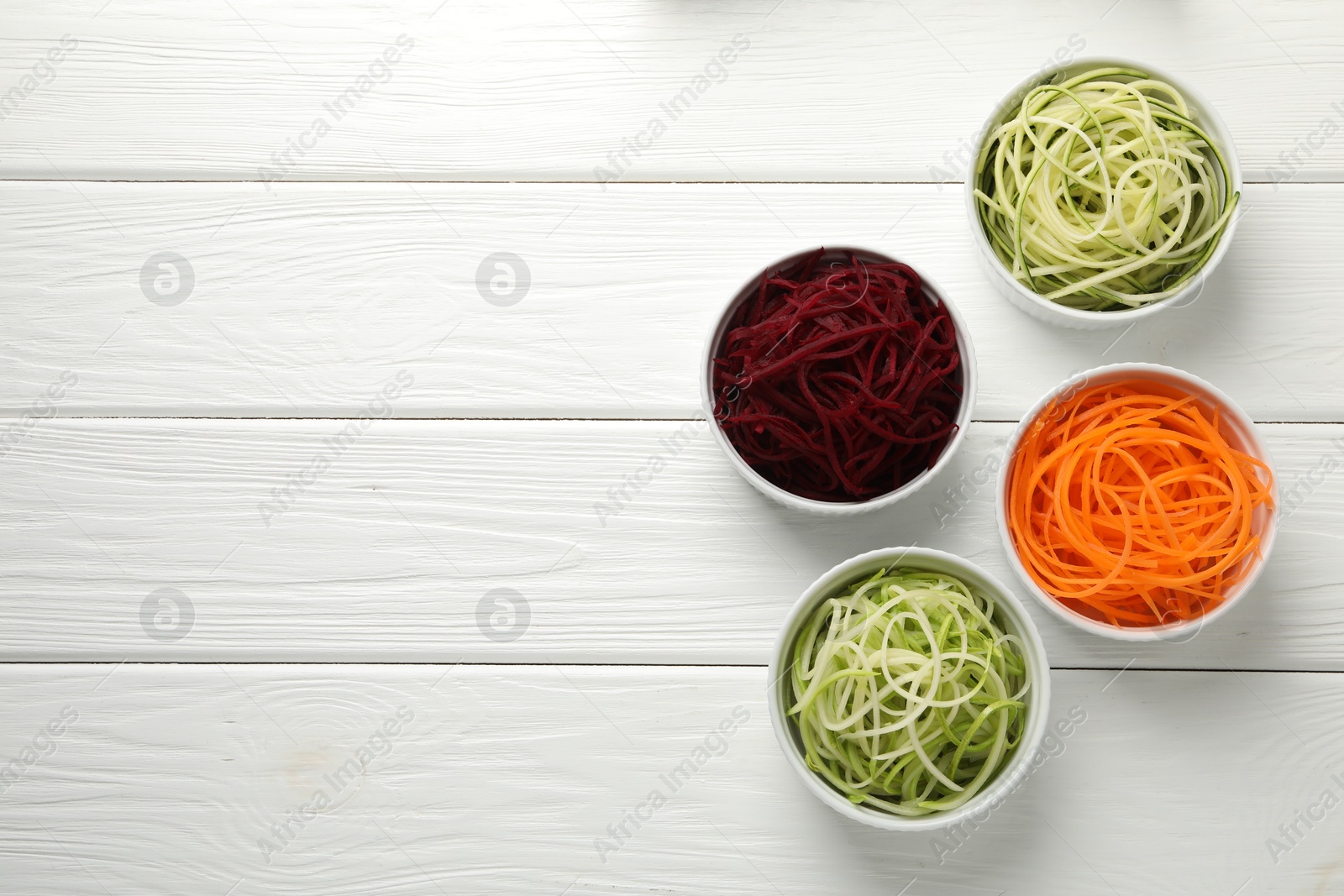 Photo of Vegetarian dish. Different vegetable noodles in bowls on white wooden table, flat lay. Space for text
