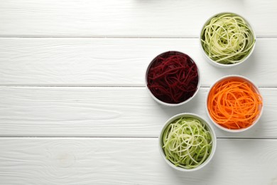 Photo of Vegetarian dish. Different vegetable noodles in bowls on white wooden table, flat lay. Space for text