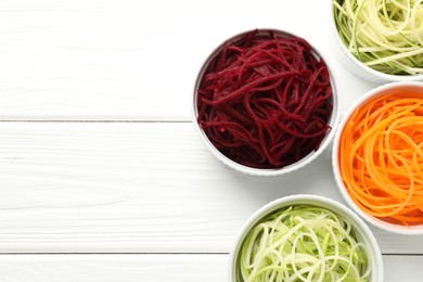 Photo of Vegetarian dish. Different vegetable noodles in bowls on white wooden table, flat lay. Space for text