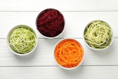 Photo of Different vegetable noodles in bowls on white wooden table, flat lay. Vegetarian dish