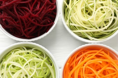 Photo of Different vegetable noodles in bowls on white wooden table, flat lay. Vegetarian dish