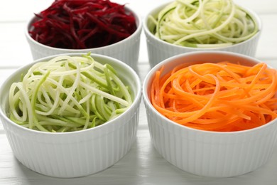 Photo of Different vegetable noodles in bowls on white wooden table, closeup. Vegetarian dish