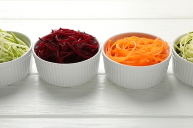 Photo of Different vegetable noodles in bowls on white wooden table, closeup. Vegetarian dish