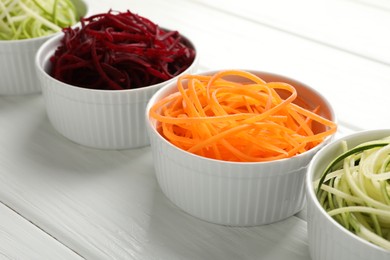 Photo of Different vegetable noodles in bowls on white wooden table, closeup. Vegetarian dish