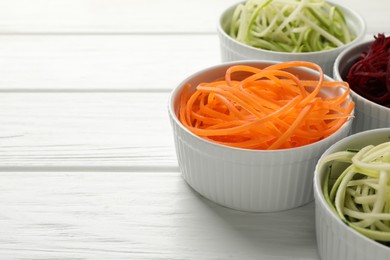 Photo of Vegetarian dish. Different vegetable noodles in bowls on white wooden table, closeup. Space for text