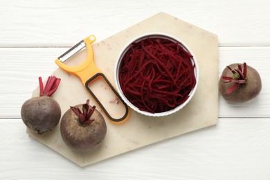 Photo of Raw beetroot noodles, fresh vegetables and peeler on white wooden table, flat lay