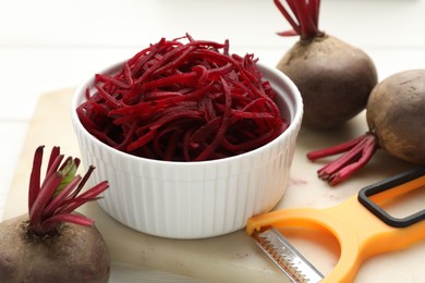 Photo of Raw beetroot noodles, fresh vegetables and peeler on table, closeup